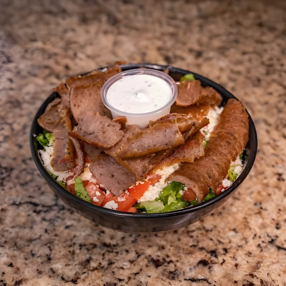 Joe's Falafel gyro bowl with sliced meat, lettuce, tomatoes, feta, and a side of sauce.