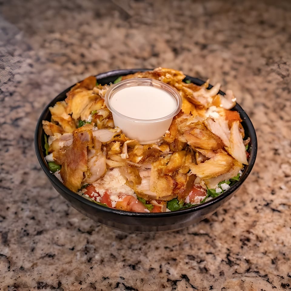 Joe's Falafel chicken shawarma bowl with lettuce, tomatoes, feta, and a side of white sauce.