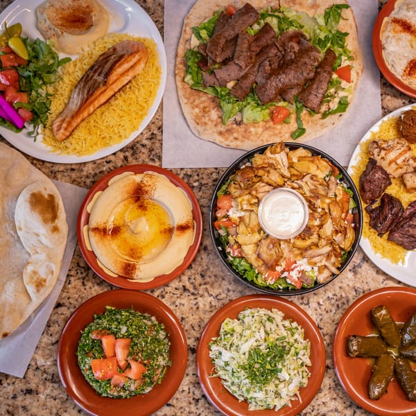 A top-down view of a spread of Joe's Falafel dishes, including salmon, shawarma, hummus, and salads.