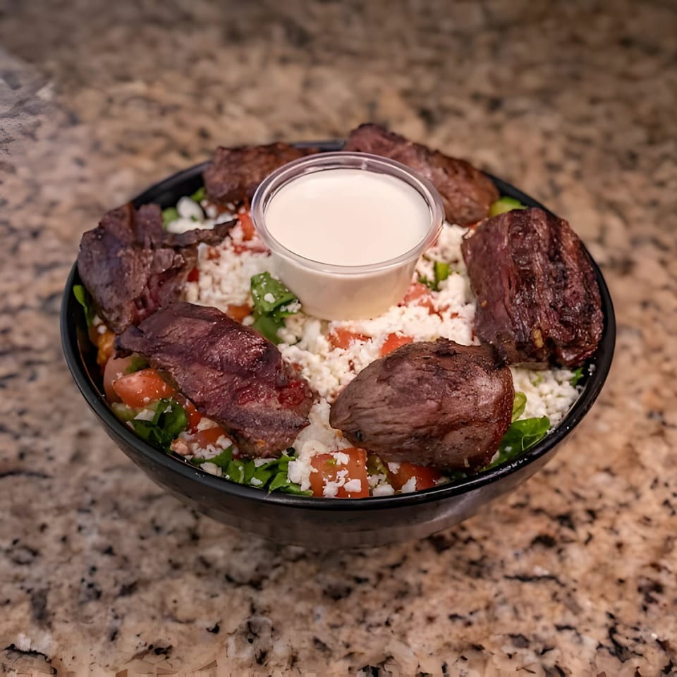 Joe's Falafel bowl with grilled meat, crumbled feta, diced tomatoes, and a side of sauce.